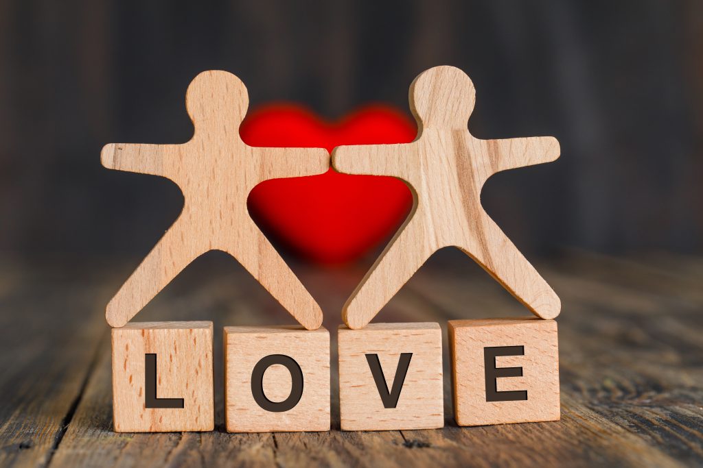 Relationship concept with red heart, wooden cubes and human models on wooden background side view